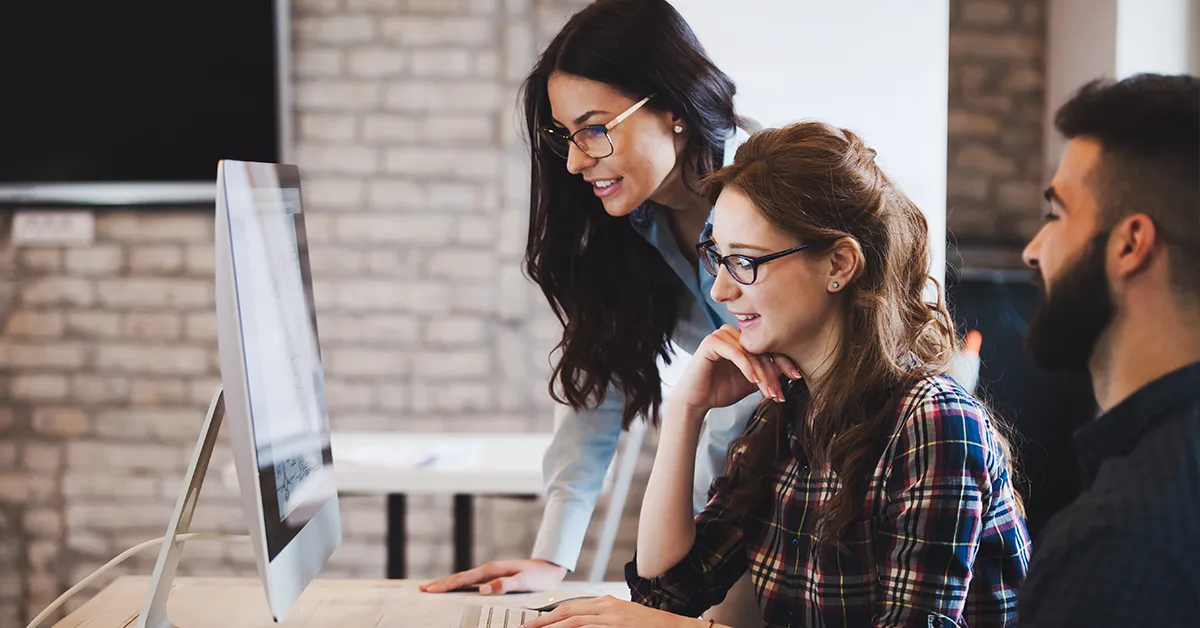 Three colleagues smiling as they review work together on a desktop computer
