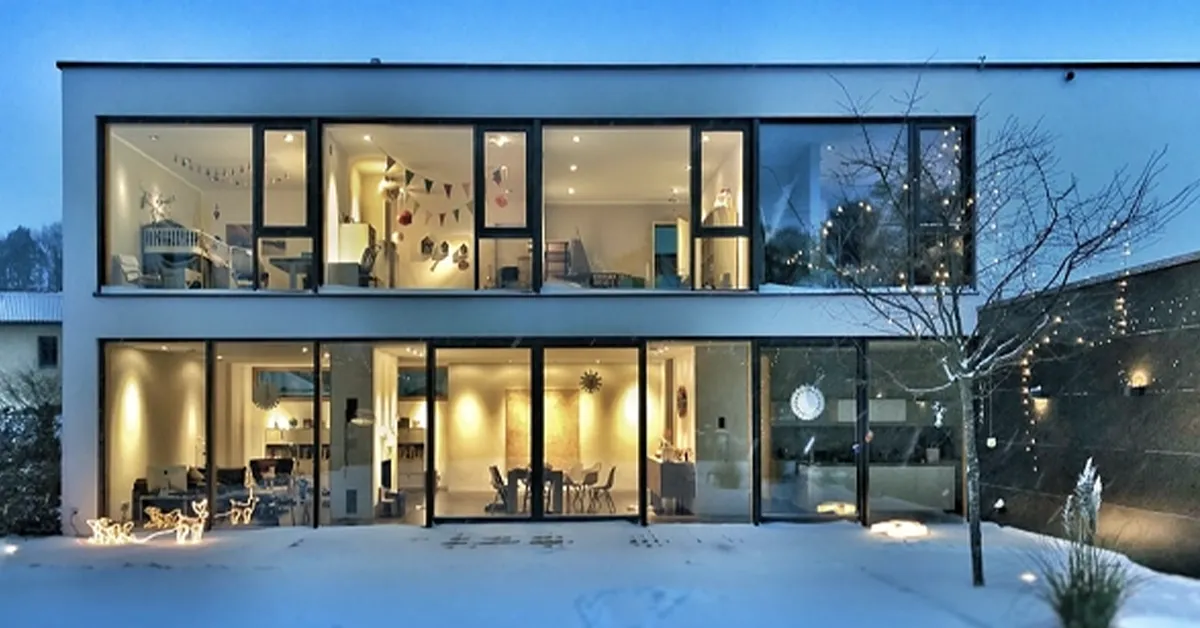 Modern two-story house with floor-to-ceiling windows lit up at dusk in the snow